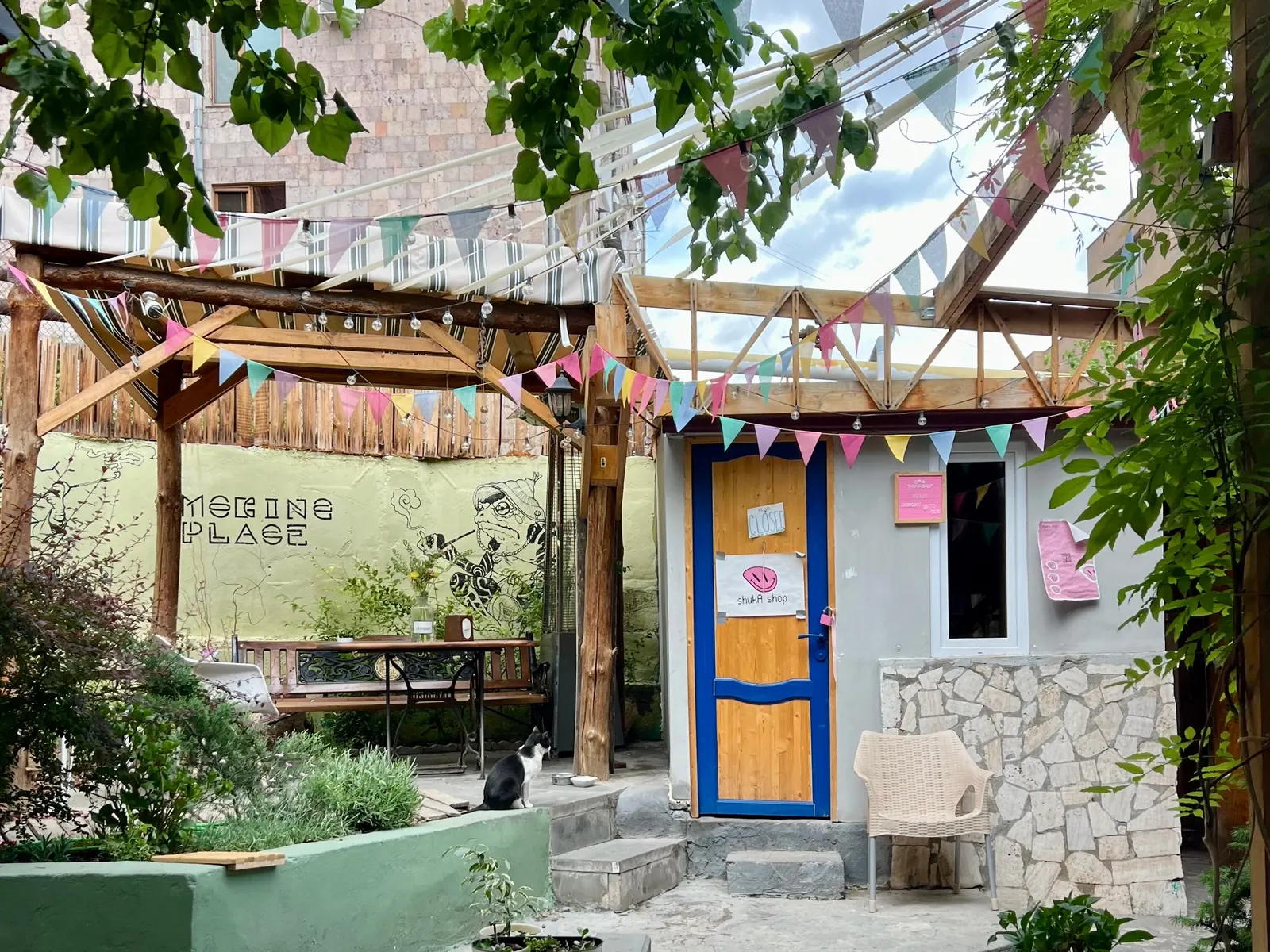 The courtyard under strings of bunting, with green planters, benches and the blue door
