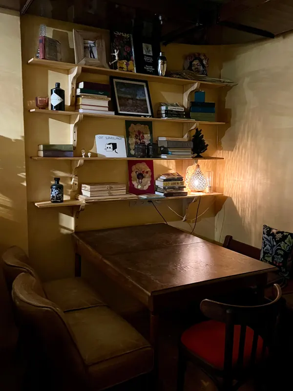 A corner table under shelves of books, pictures and a glowing lamp