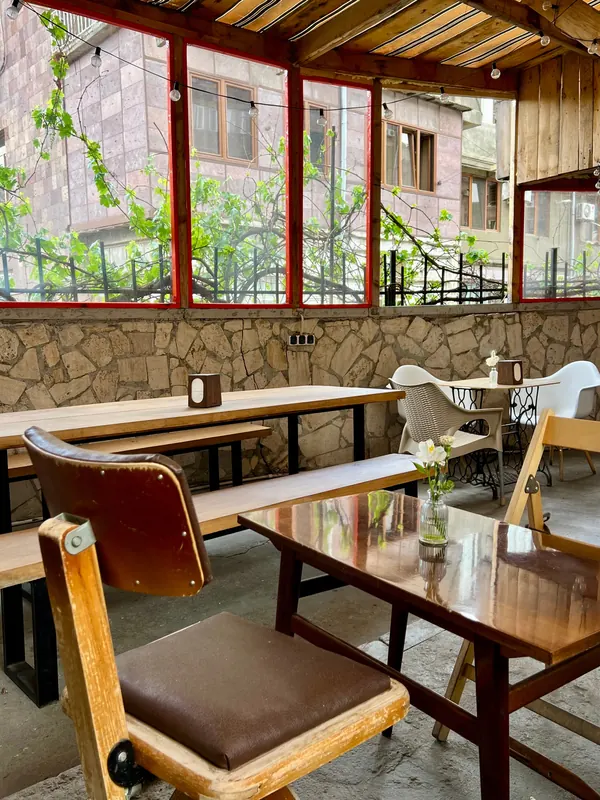The glazed terrace: wooden tables, a leather chair and a vine at the window